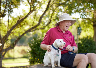 Man in a sun hat sitting outside with a medium sized white dog.