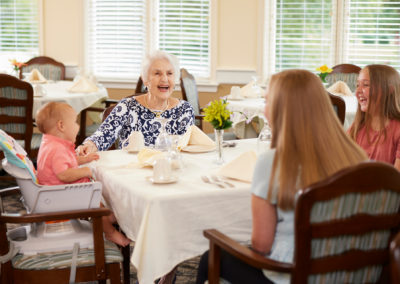 Woman siting at a dining table with younger family members and a baby in a highchair.