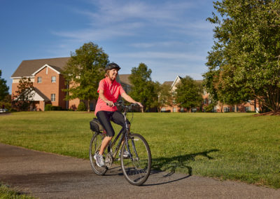 woman riding a bike down a paved trail surrounded by a large greenspace