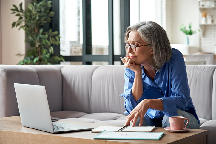 senior woman watching a video on her laptop while sitting on her living room couch