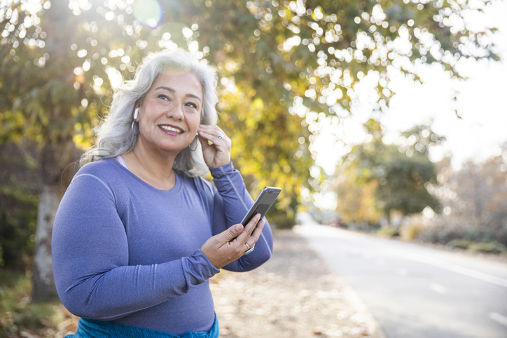 elderly woman holding her smartphone while adjusting her air-pods